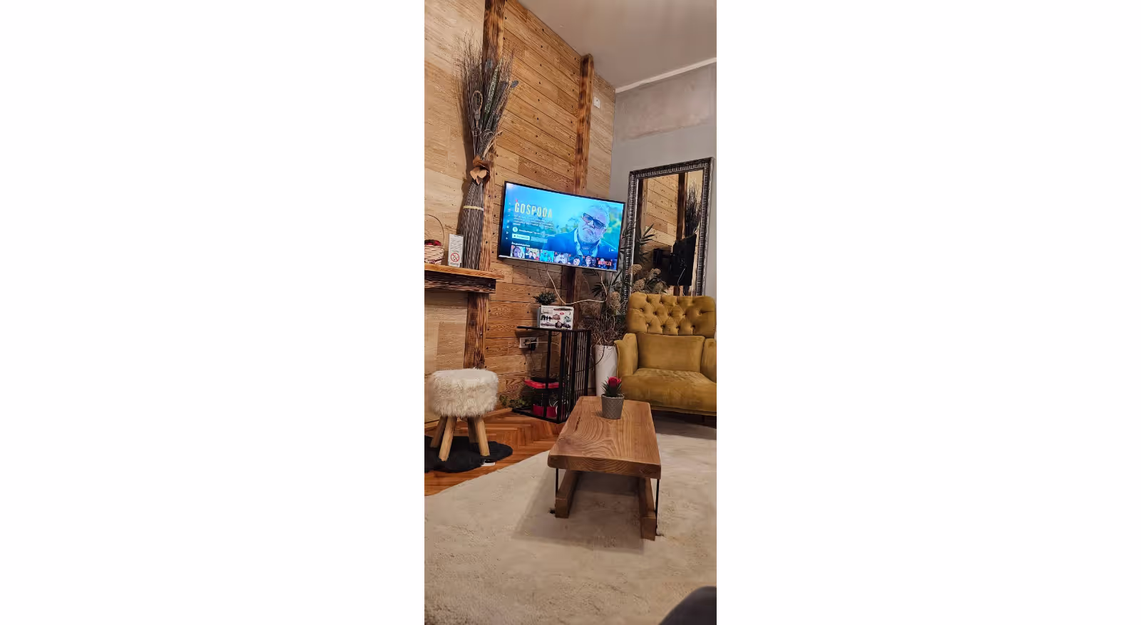 Elegantna dnevna soba sa televizorom, ogledalom i rustičnim detaljima.